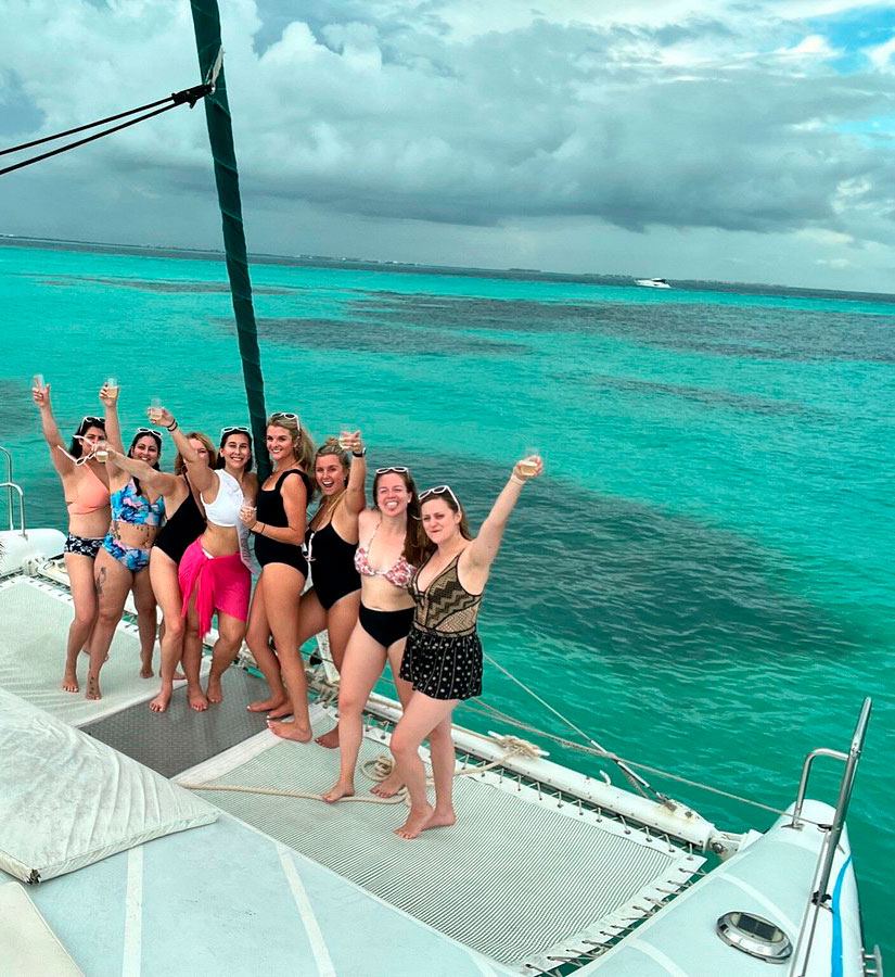 Group celebrating on the catamaran bow over turquoise water